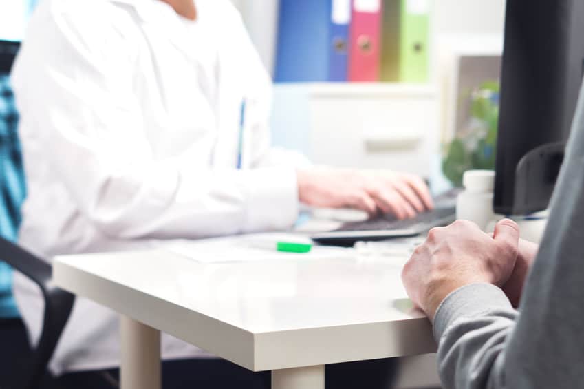 A multi-tasking doctor trying to fill out an EMR while talking with a patient. Clinical burnout is on the rise in part due to the time needed to update EMRs.