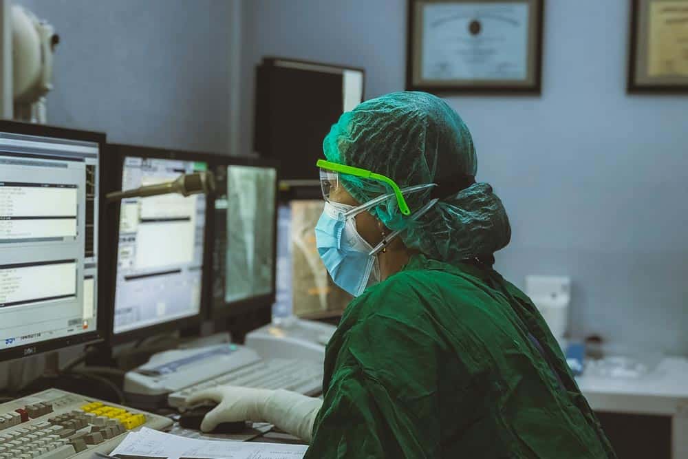 Gowned-up doctor has to stop and enter patient data into the EMR, wasting valuable patient interaction and clinician time.