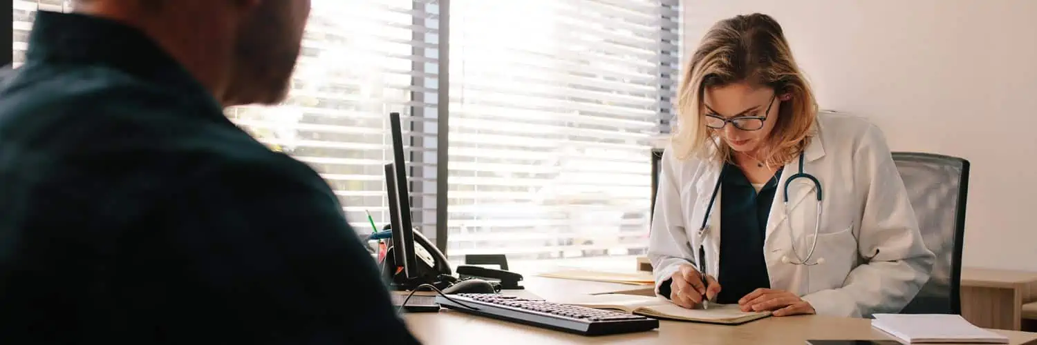 Doctor ignoring patient while writing notes. Virtual medical scribes can improve facetime and reduce clerical duties.