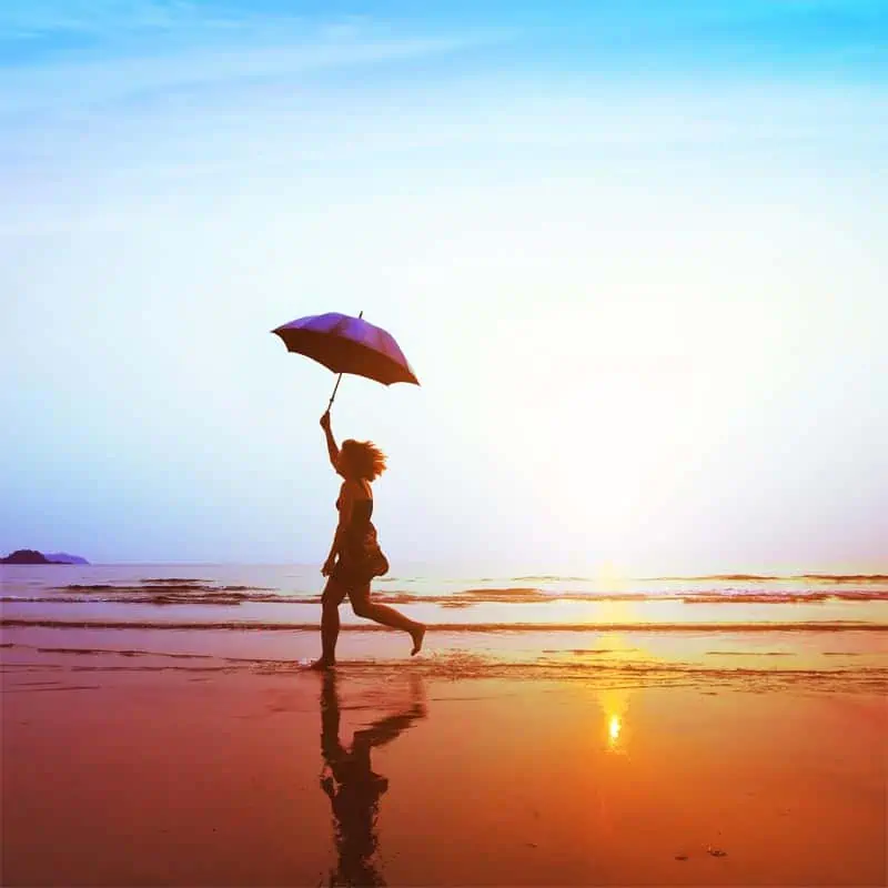 Woman with an umbrella running down the beach signifying happy insurance customer.